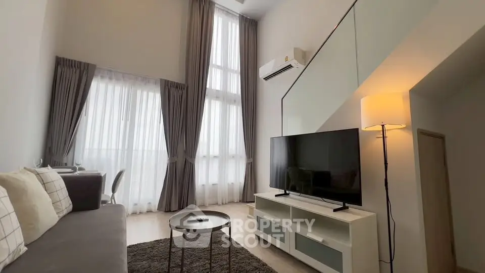 Modern living room with high ceilings and large windows, featuring a cozy sofa and sleek TV setup.