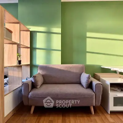 Cozy living room with stylish gray sofa and wooden shelving against green walls.