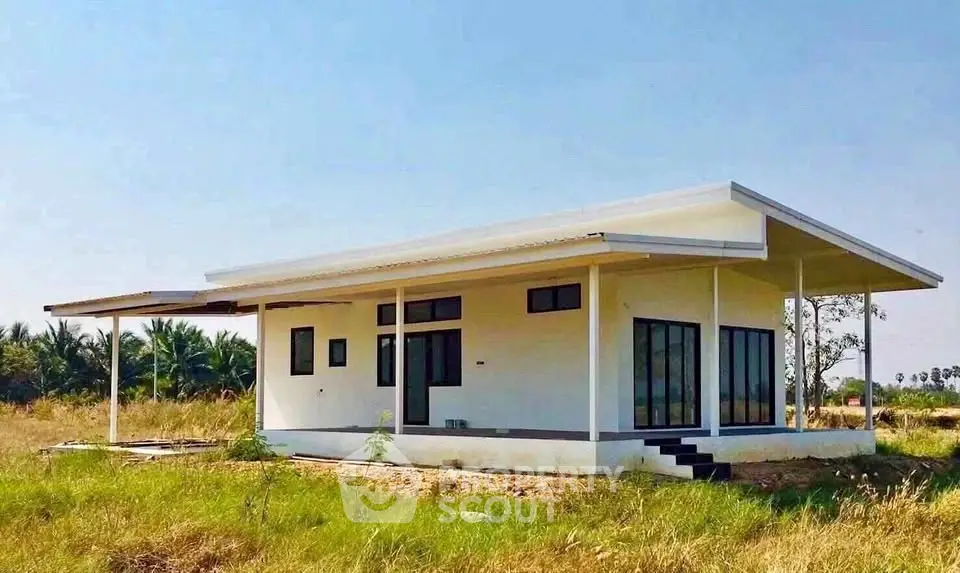 Modern minimalist single-story house with large windows and sloped roof in a serene rural setting.