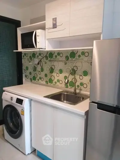 Compact modern kitchen with washing machine, microwave, and fridge in stylish apartment.