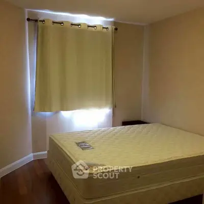 Cozy bedroom with natural light and wooden flooring, featuring a comfortable mattress and elegant curtains.