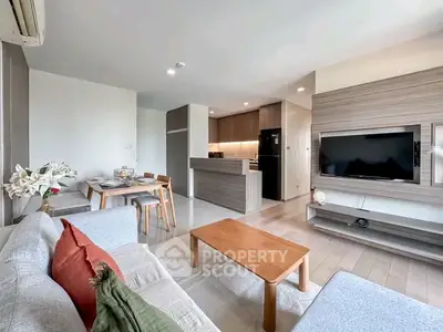 Modern living room with open kitchen, stylish furniture, and large TV in a cozy apartment.