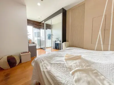 Spacious bedroom with modern decor and balcony access, featuring wooden flooring and ample natural light.