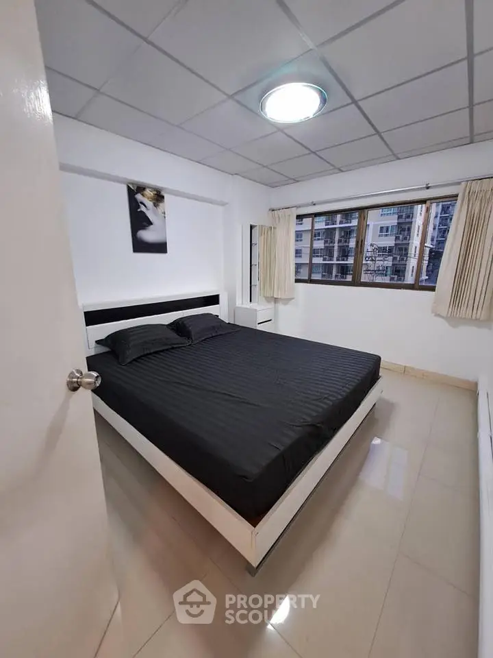 Modern bedroom with sleek black bedding and city view window in stylish apartment.