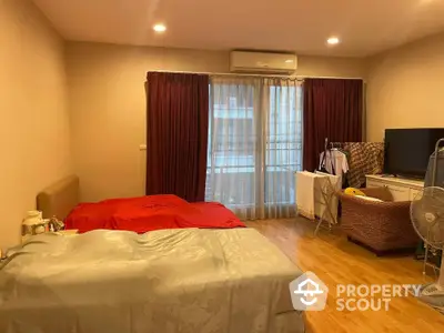 Spacious bedroom with hardwood flooring, large windows draped with maroon curtains, and ample natural light, perfect for relaxation and comfort.