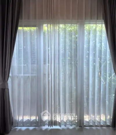 Elegant window with sheer curtains offering a serene garden view, perfect for tranquil living spaces.