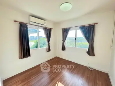 Bright empty room with wooden flooring and large windows offering scenic views.