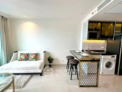 Modern open-plan living room with stylish kitchen and washing machine, featuring elegant decor and natural light.