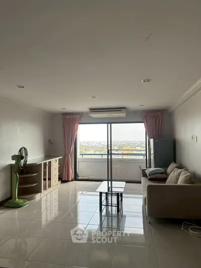 Spacious living room with large window offering stunning city views, featuring modern furniture and tiled flooring.