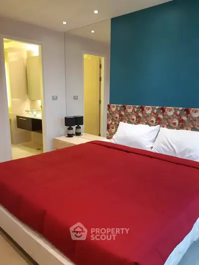 Modern bedroom with vibrant red bedding and stylish decor adjacent to a sleek bathroom.