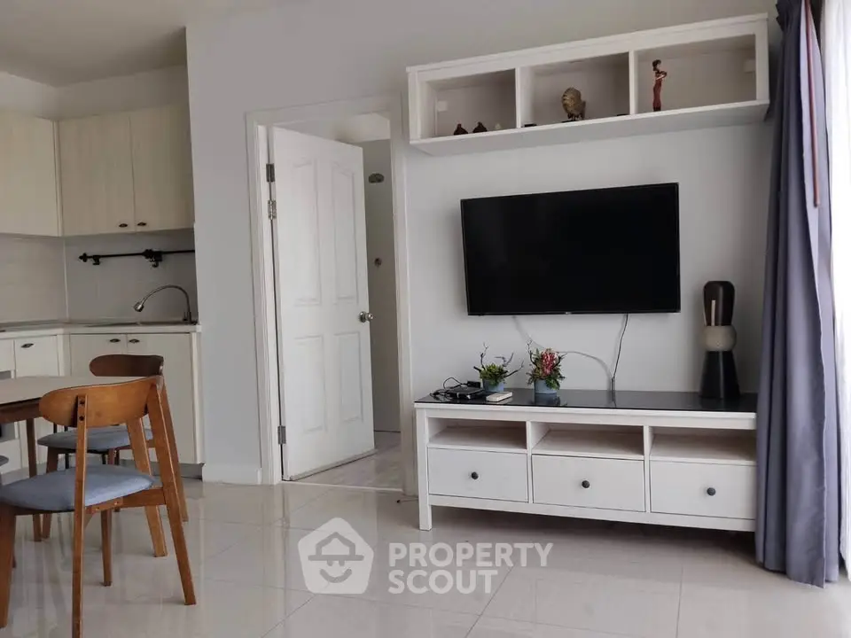 Modern living room with wall-mounted TV and open kitchen layout, featuring stylish furniture and decor.