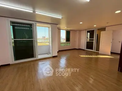 Spacious living room with large windows and wooden flooring, offering abundant natural light and city views.