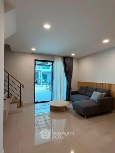 Modern living room with sleek design and natural light, featuring a stylish sofa and elegant staircase.