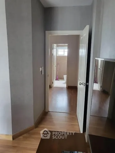 Modern interior hallway leading to a bathroom with wooden flooring and neutral walls.