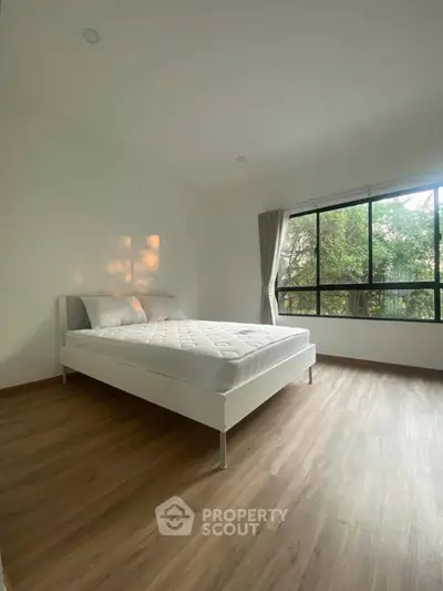 Spacious bedroom with large window and natural light, featuring a minimalist design and wooden flooring.