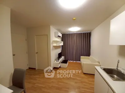 Modern living room with wooden flooring, white sofa, and compact kitchen area.