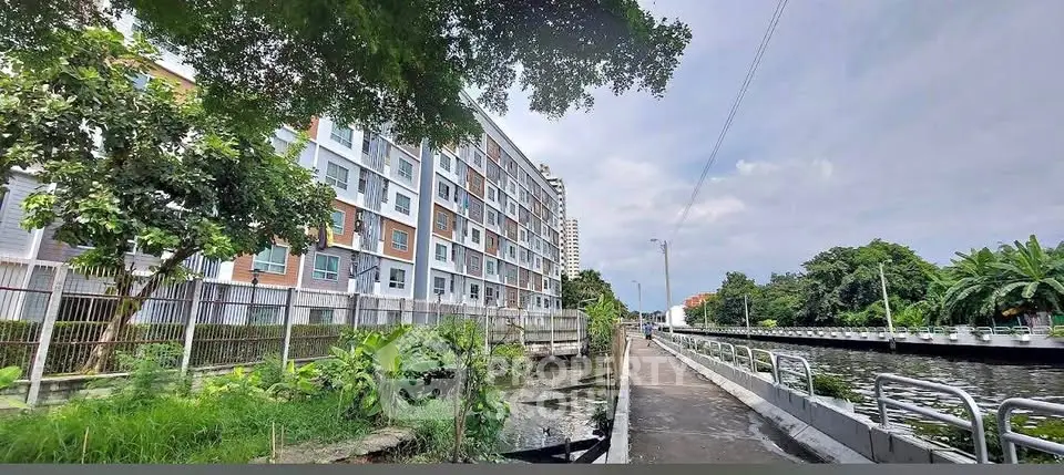 Modern riverside apartment building with lush greenery and scenic canal view.