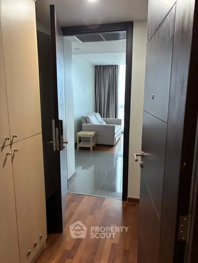 Modern apartment entrance leading to a cozy living room with wooden flooring and natural light.