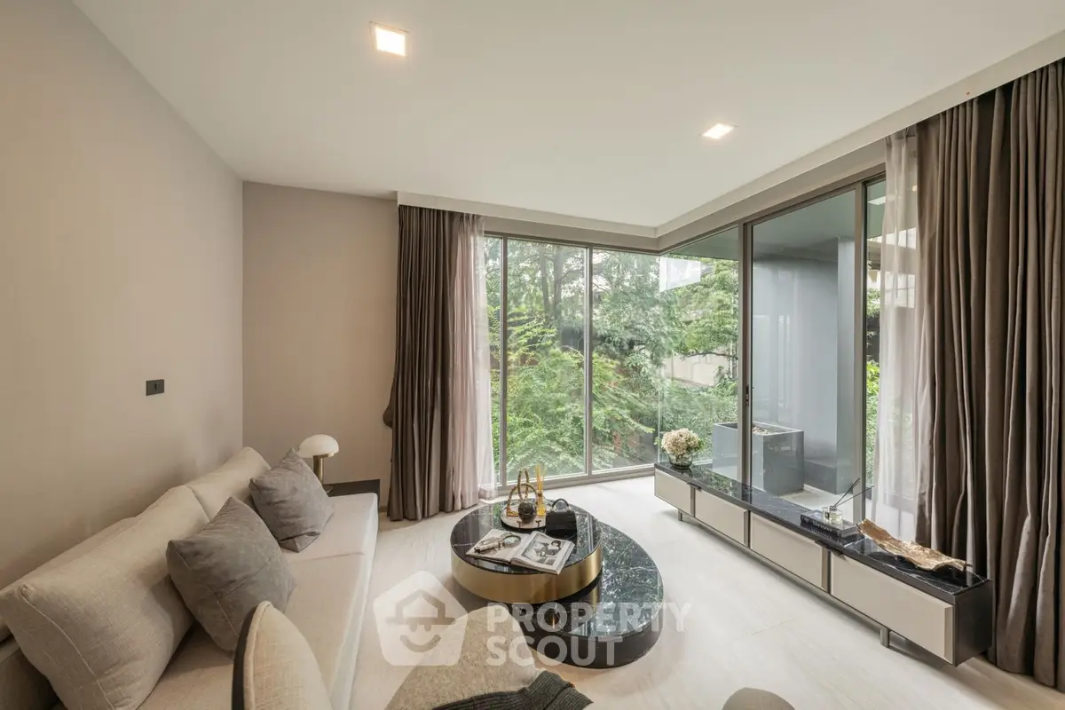 Luxurious living room with floor-to-ceiling windows and modern decor overlooking lush greenery.