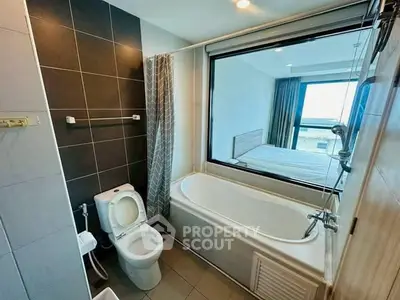 Modern bathroom with bathtub and large window overlooking bedroom, featuring sleek tiles and contemporary fixtures.