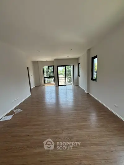 Spacious empty living room with hardwood floors and large windows offering natural light.