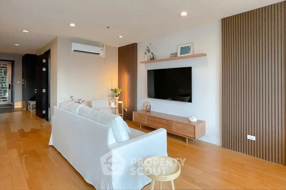 Modern living room with wooden flooring, stylish furniture, and wall-mounted TV in a cozy apartment.