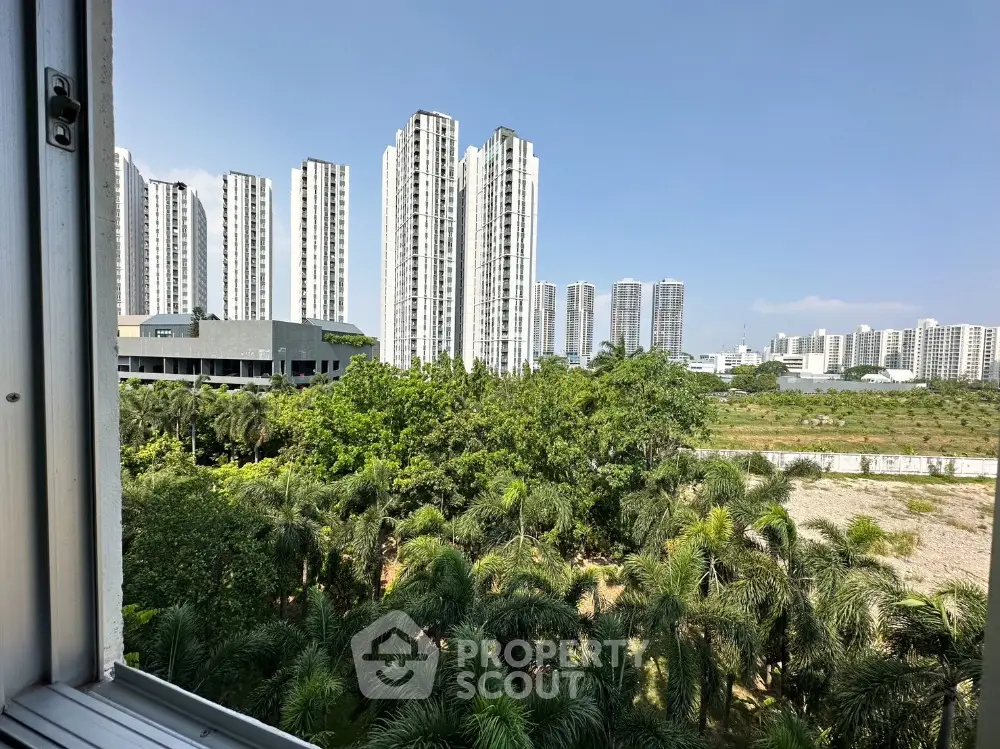 Stunning cityscape view from a high-rise window overlooking lush greenery and modern skyscrapers.
