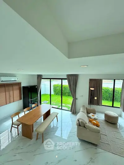 Spacious modern living room with large windows and garden view, featuring elegant furniture and natural light.