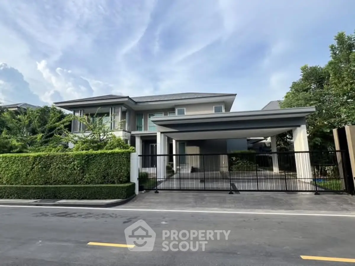 Modern luxury home with sleek design and spacious driveway, surrounded by lush greenery and clear blue skies.