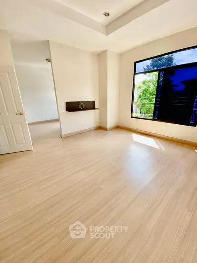 Spacious and bright room with large window and modern flooring, perfect for versatile living space.