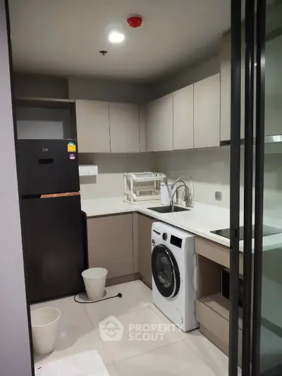 Modern kitchen with sleek cabinetry, washing machine, and spacious fridge in a contemporary apartment.