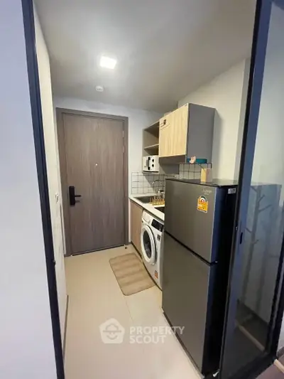 Compact modern kitchen with washing machine and fridge in a cozy apartment.