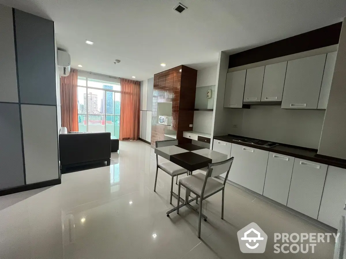 Spacious modern kitchen with sleek white cabinetry and high-gloss flooring, extending into a cozy living area with ample natural light.