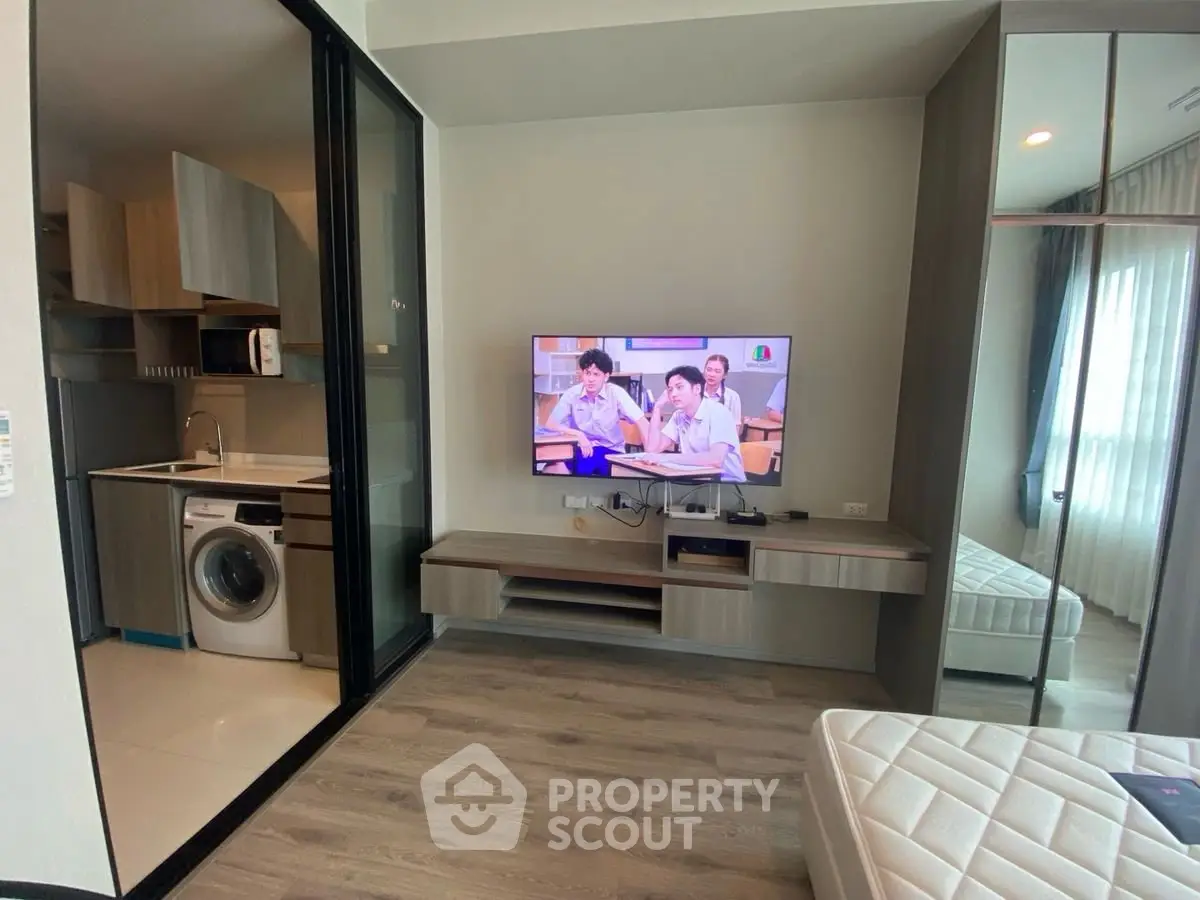 Modern apartment interior with open kitchen and living area featuring a wall-mounted TV and washing machine.