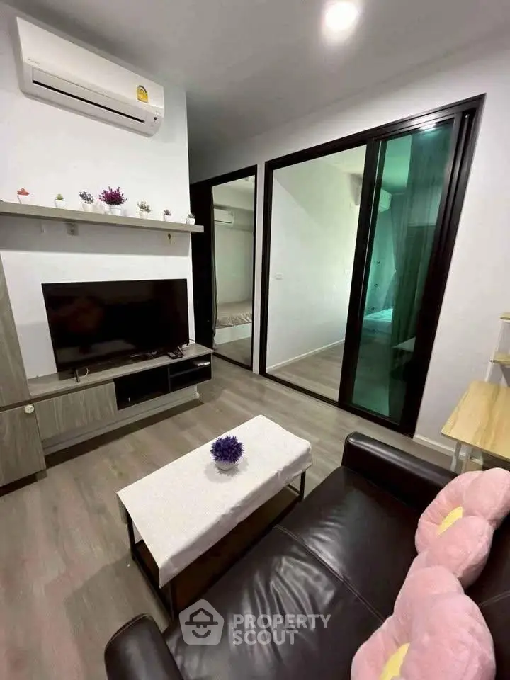 Modern living room with sleek design, featuring a black leather sofa, wall-mounted TV, and sliding glass doors.