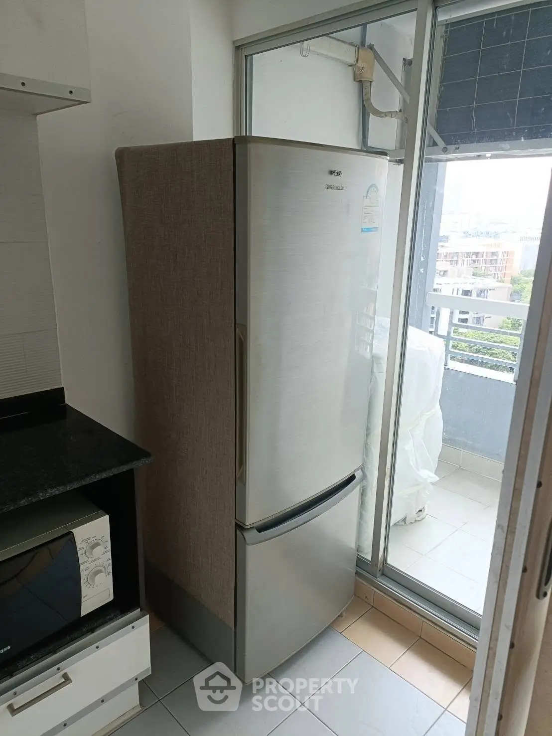 Modern kitchen with sleek fridge and microwave near balcony with city view.