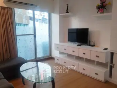 Modern living room with sleek TV unit and glass coffee table, featuring large window for natural light.