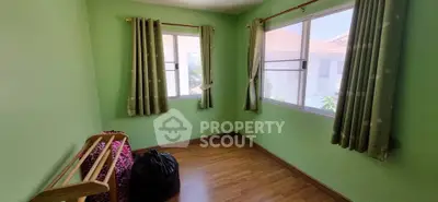 Bright green room with wooden floor and large windows, perfect for a cozy bedroom or study.