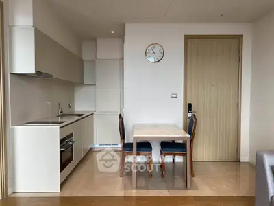 Modern kitchen with dining area and wooden door, featuring sleek cabinetry and a wall clock.
