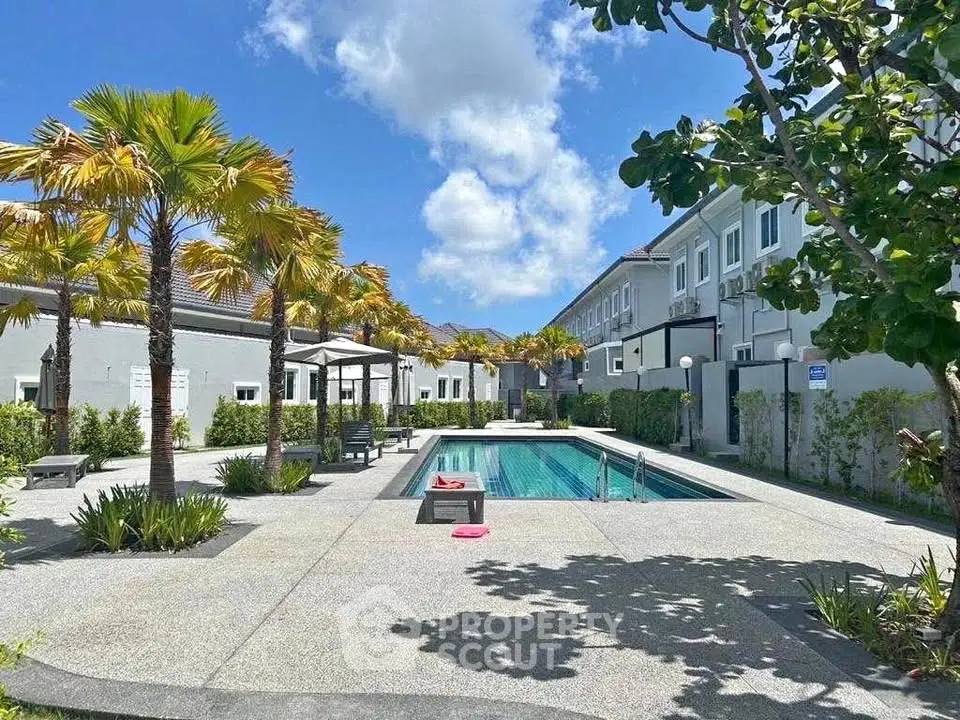 Luxurious residential pool area with palm trees and modern architecture under a clear blue sky.