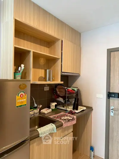 Compact kitchen with wooden cabinets and stainless steel fridge in modern apartment