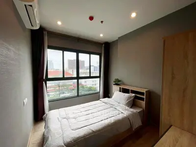 Cozy bedroom with large window and city view, featuring modern furnishings and natural light.