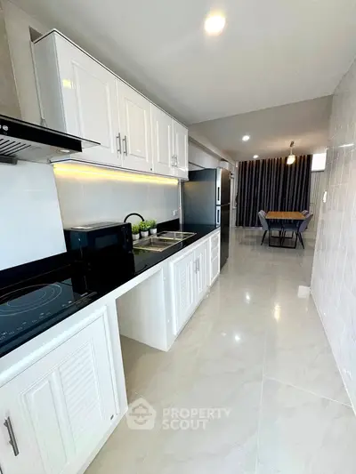 Modern kitchen with sleek white cabinets and open layout leading to dining area.