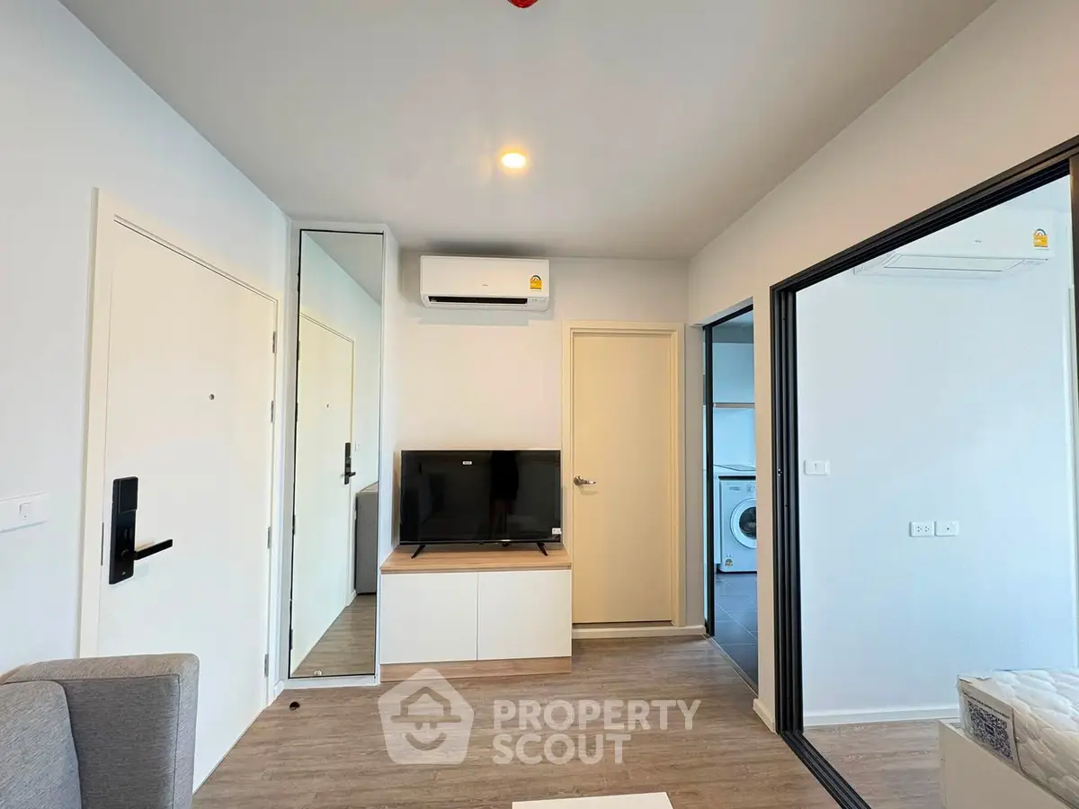 Modern living room with sleek design, featuring a wall-mounted TV, air conditioning, and a glimpse of a laundry area.
