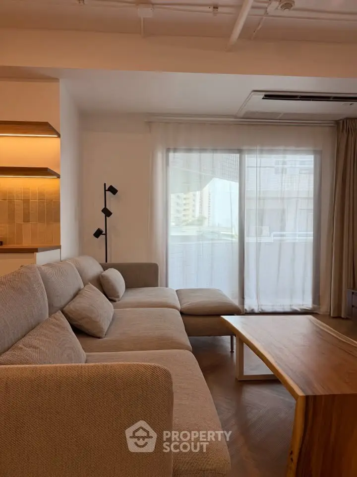 Modern living room with cozy sectional sofa and wooden coffee table, featuring large window with city view.