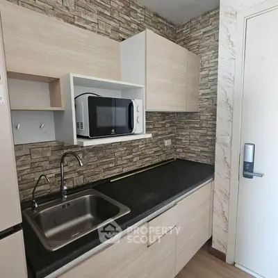 Modern kitchen with sleek cabinetry and microwave, featuring a stylish stone backsplash.
