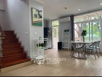 Spacious modern living room with dining area and staircase, featuring large windows and stylish decor.