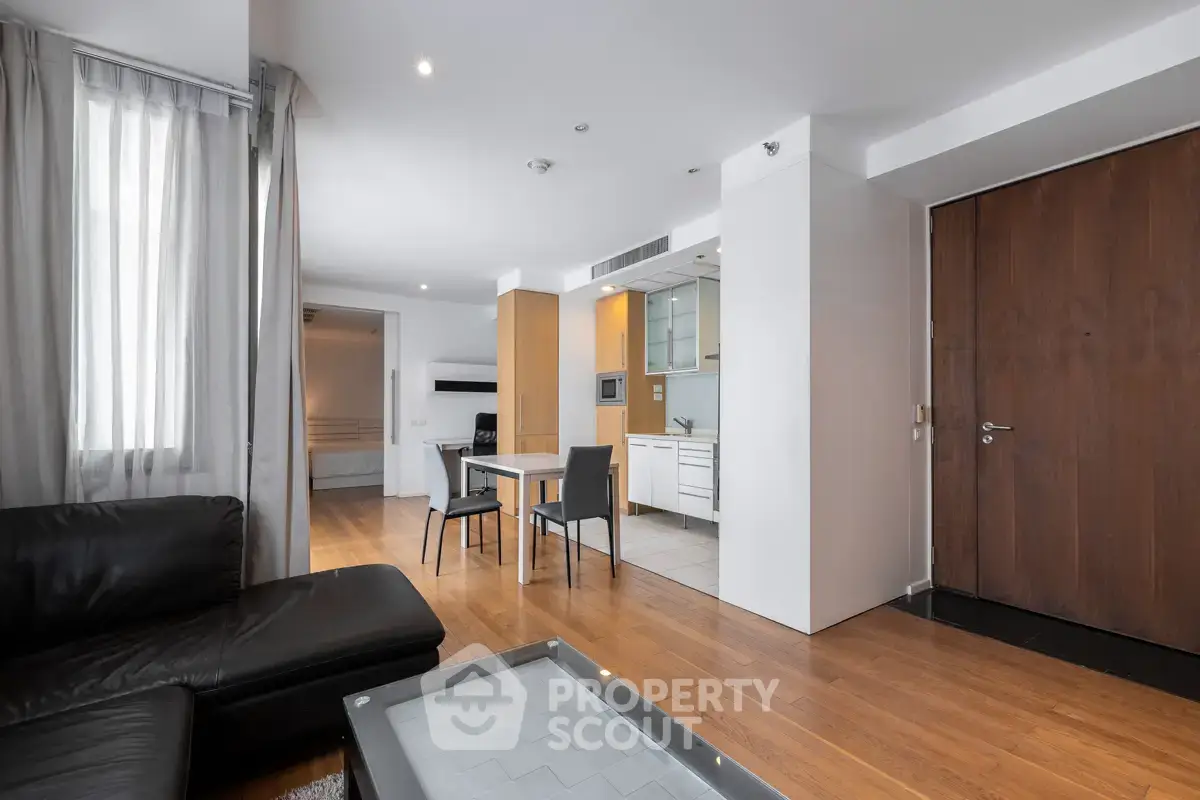Modern open-plan living room with sleek kitchen and dining area, featuring hardwood floors and contemporary furniture.