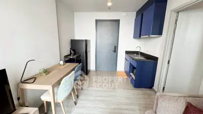 Modern compact living space with kitchenette and dining area, featuring sleek blue cabinetry and minimalist decor.