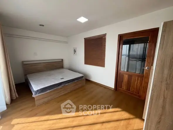 Spacious bedroom with wooden flooring and large window for natural light.